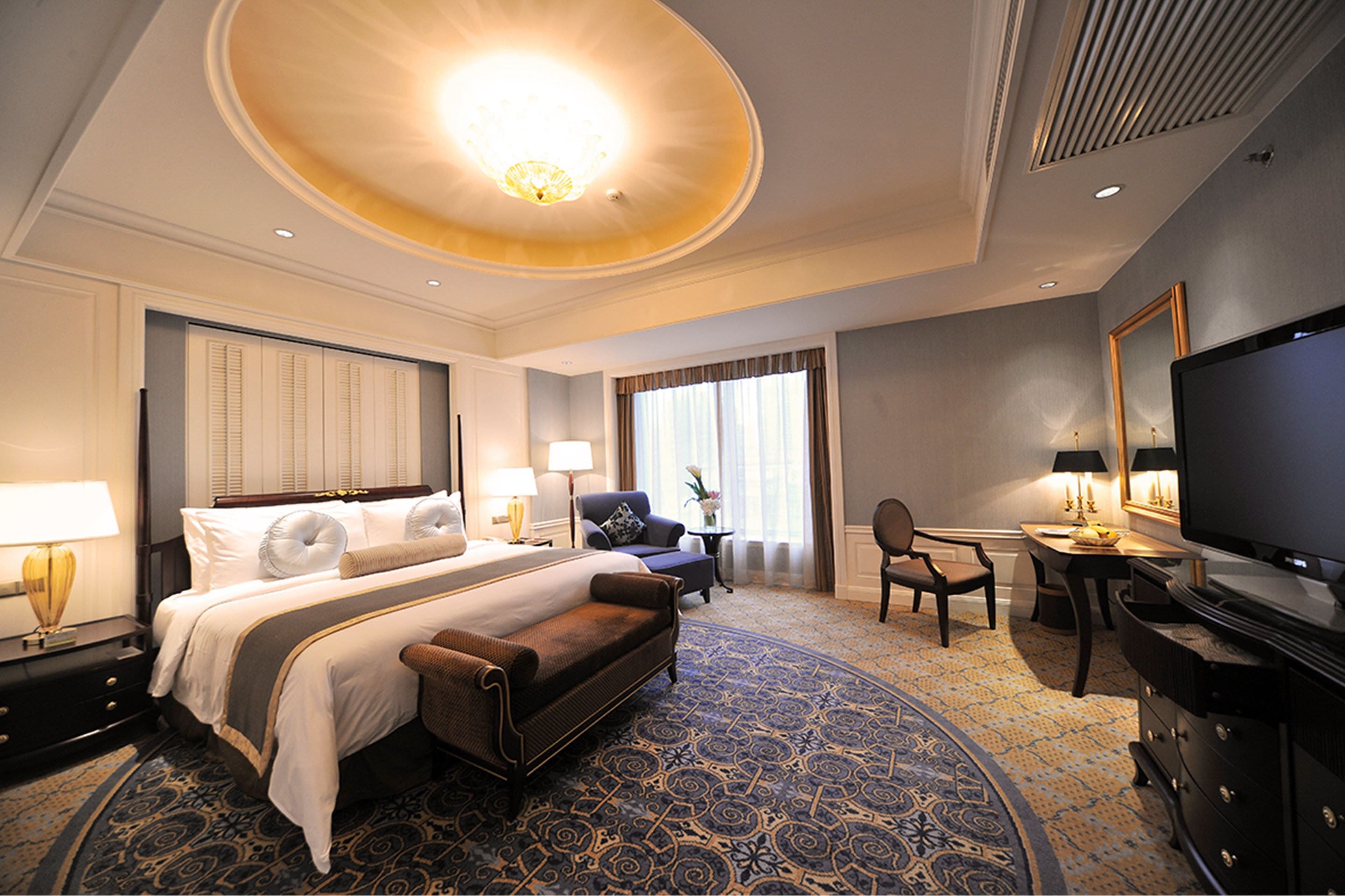 A hotel room with a large bed, a sofa, a desk with a TV, and a chair.