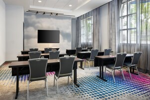 Sala de conferências com uma grande tela de televisão, várias mesas e cadeiras.
