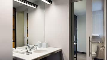 Une salle de bain moderne avec un lavabo blanc, un miroir et une porte en verre donnant accès aux toilettes.