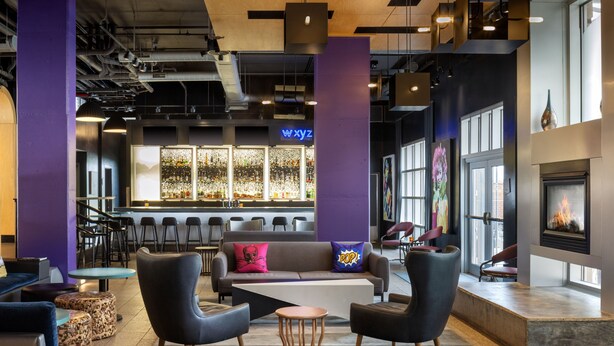A modern lounge area with a bar, seating, and a fireplace. - Aloft by Marriott Tallahassee Downtown (Tallahassee)