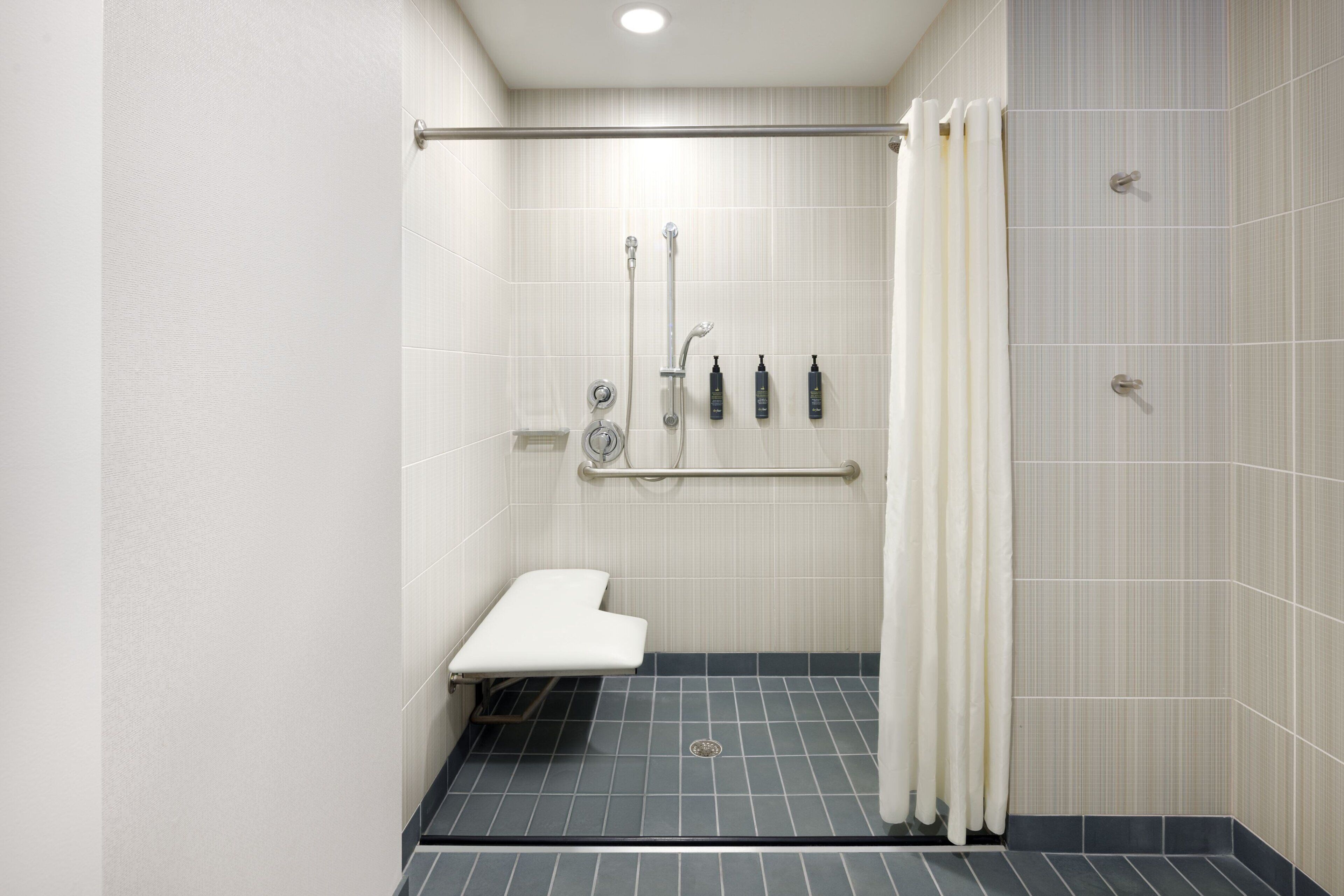 Een compacte, moderne badkamer met een douche, een bankje en een handgreep.