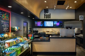 A modern coffee shop interior with a counter, beverage display, and digital menu boards. - Aloft by Marriott Tallahassee Downtown (Tallahassee)