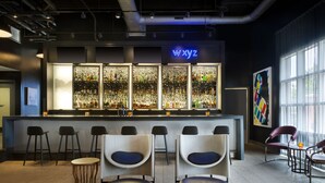 A bar area with a neon sign, bar stools, and a seating area with chairs and ottomans. - Aloft by Marriott Tallahassee Downtown (Tallahassee)