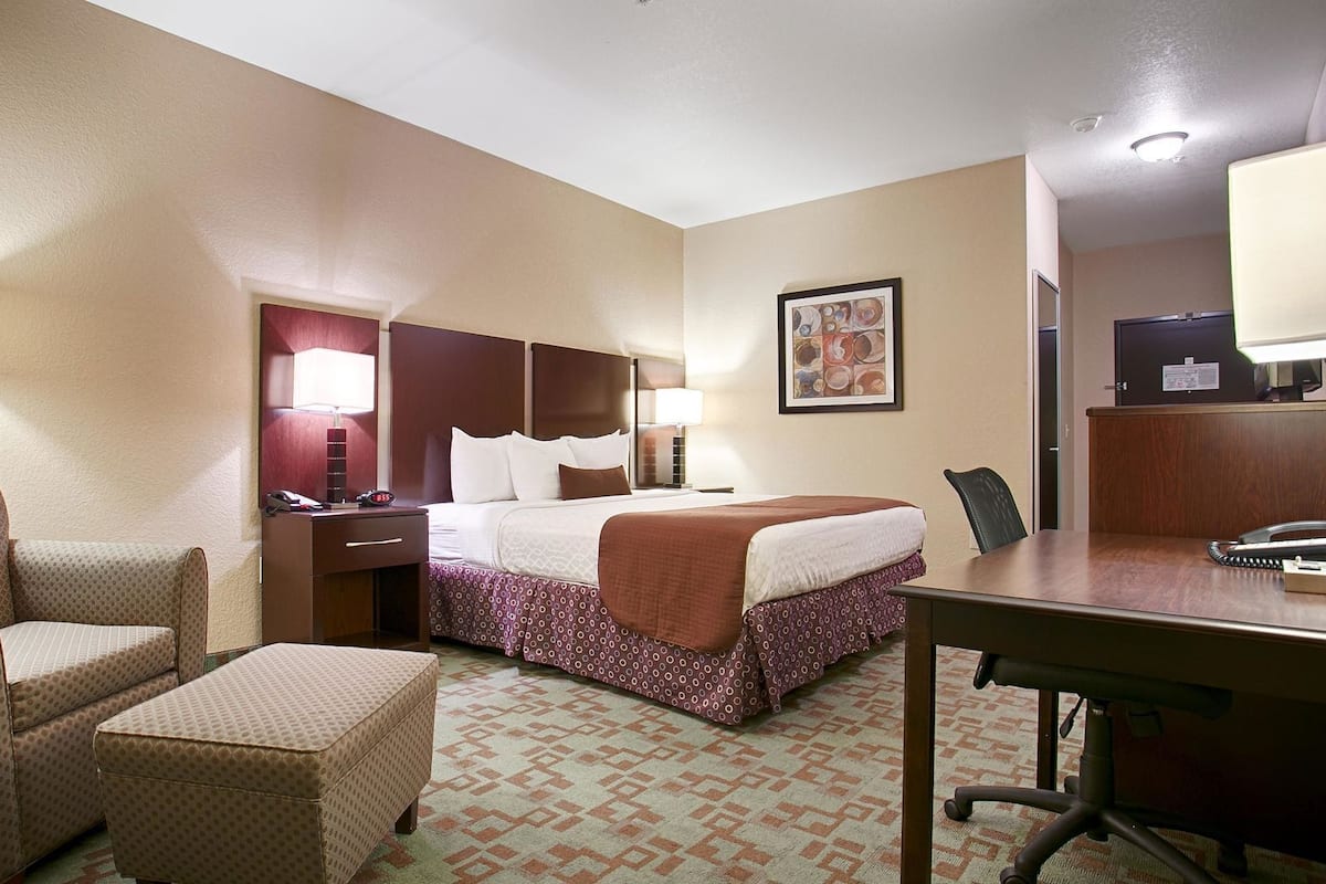 A hotel room with a bed, a desk, a chair, a nightstand, and a lamp.