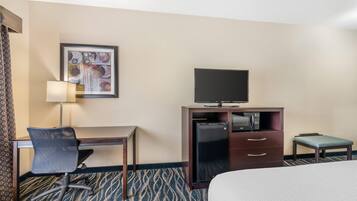 Una habitación de hotel con cama, escritorio y silla, televisor, refrigerador y una mesita.