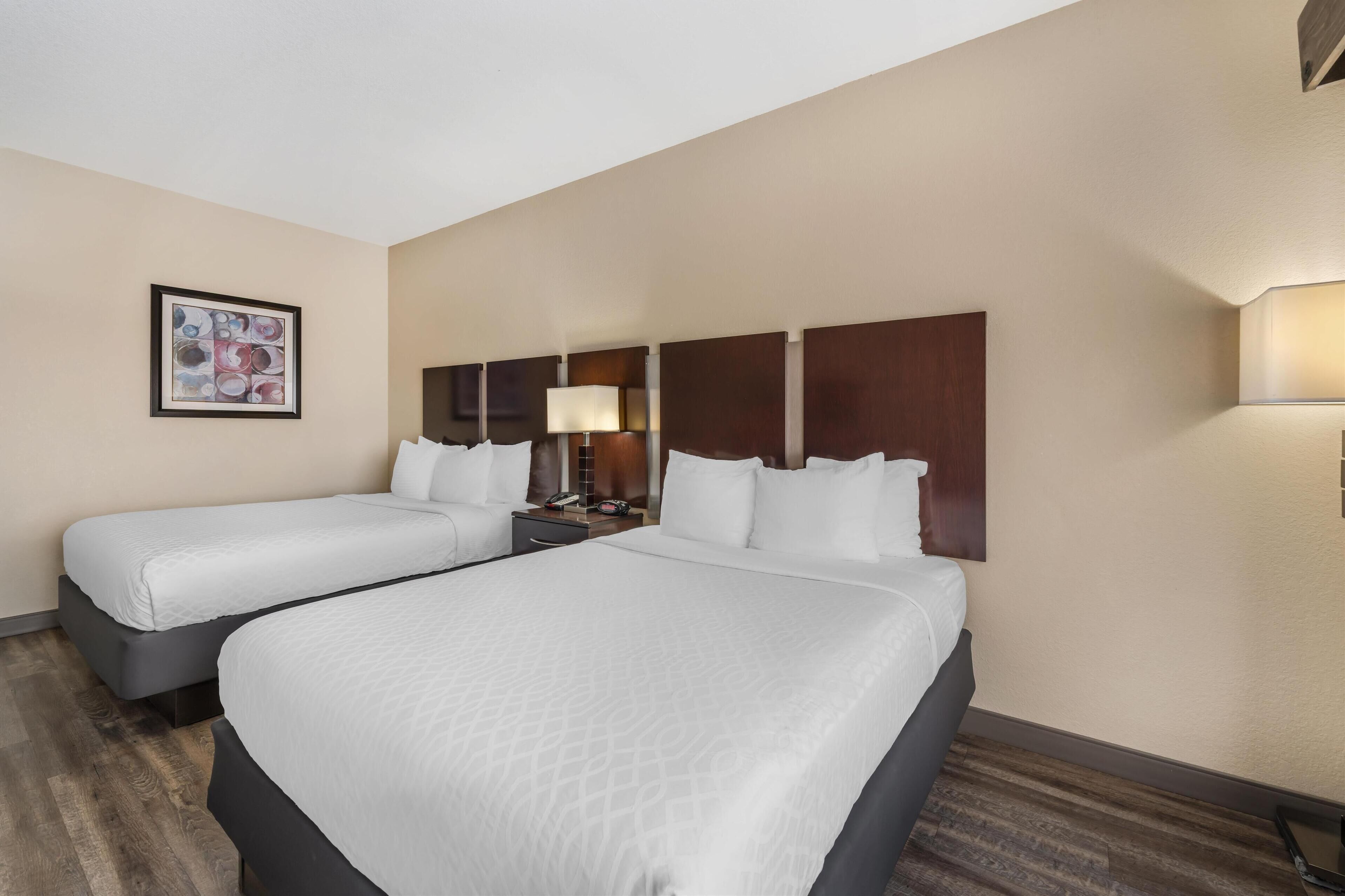 A hotel room with two beds, a nightstand with a lamp, and a framed artwork on the wall.