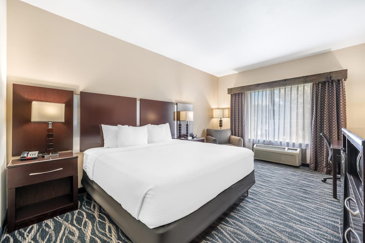 A hotel room with a large bed, bedside tables, a desk, a chair, and a window with curtains.