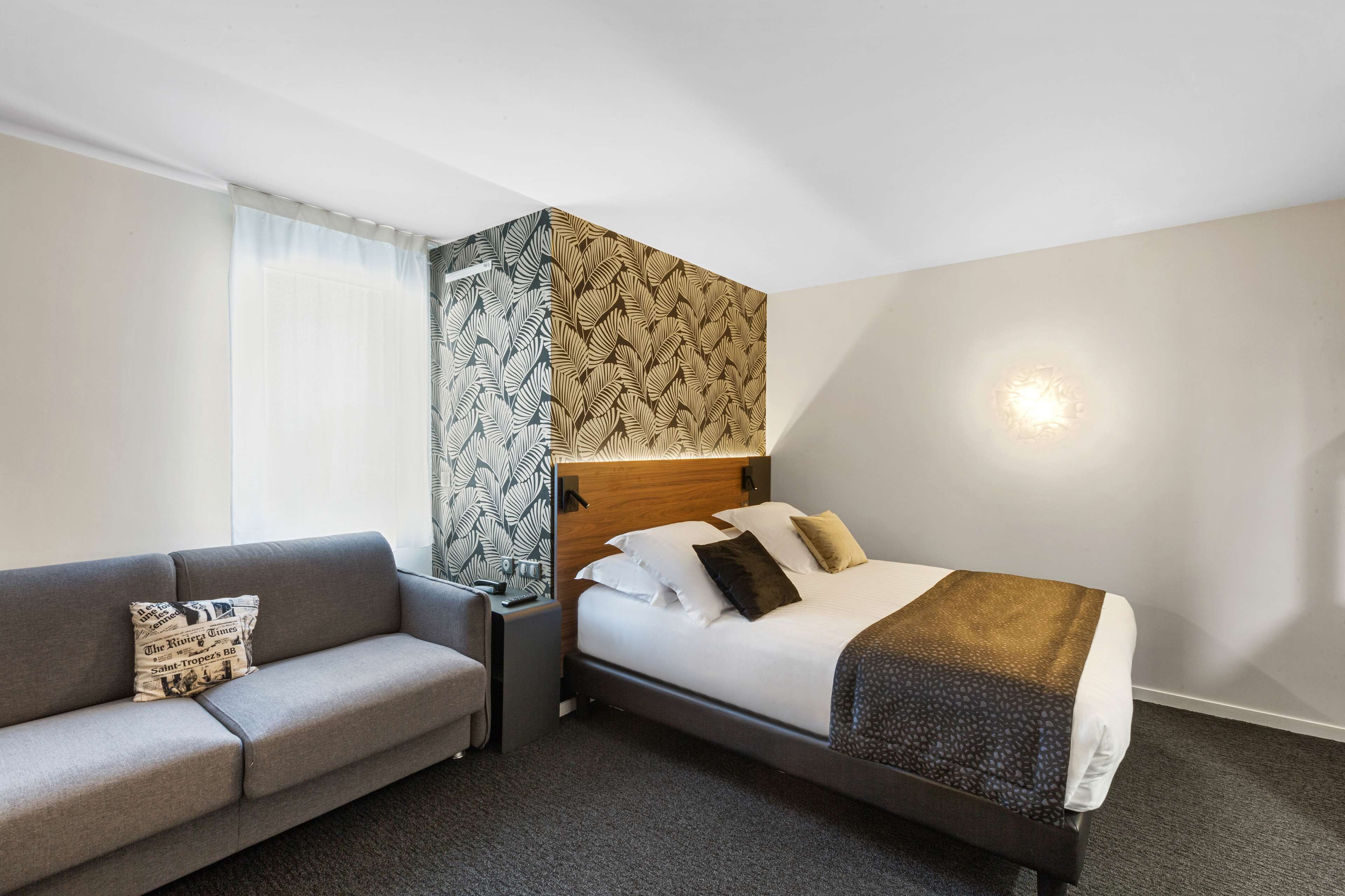 Habitación de hotel con cama, sofá, mesita de noche y una pared con estampado de hojas.