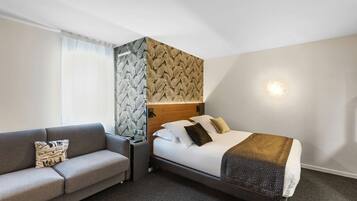 Habitación de hotel con cama, sofá, mesita de noche y una pared con estampado de hojas.