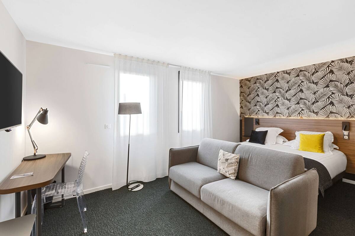 Quarto de hotel com sofá, cama, escrivaninha e cadeira.