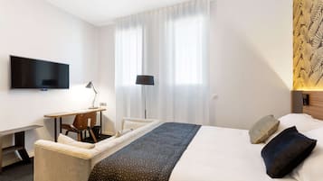 Habitación de hotel con cama, escritorio, silla, televisor y ventana con cortinas.