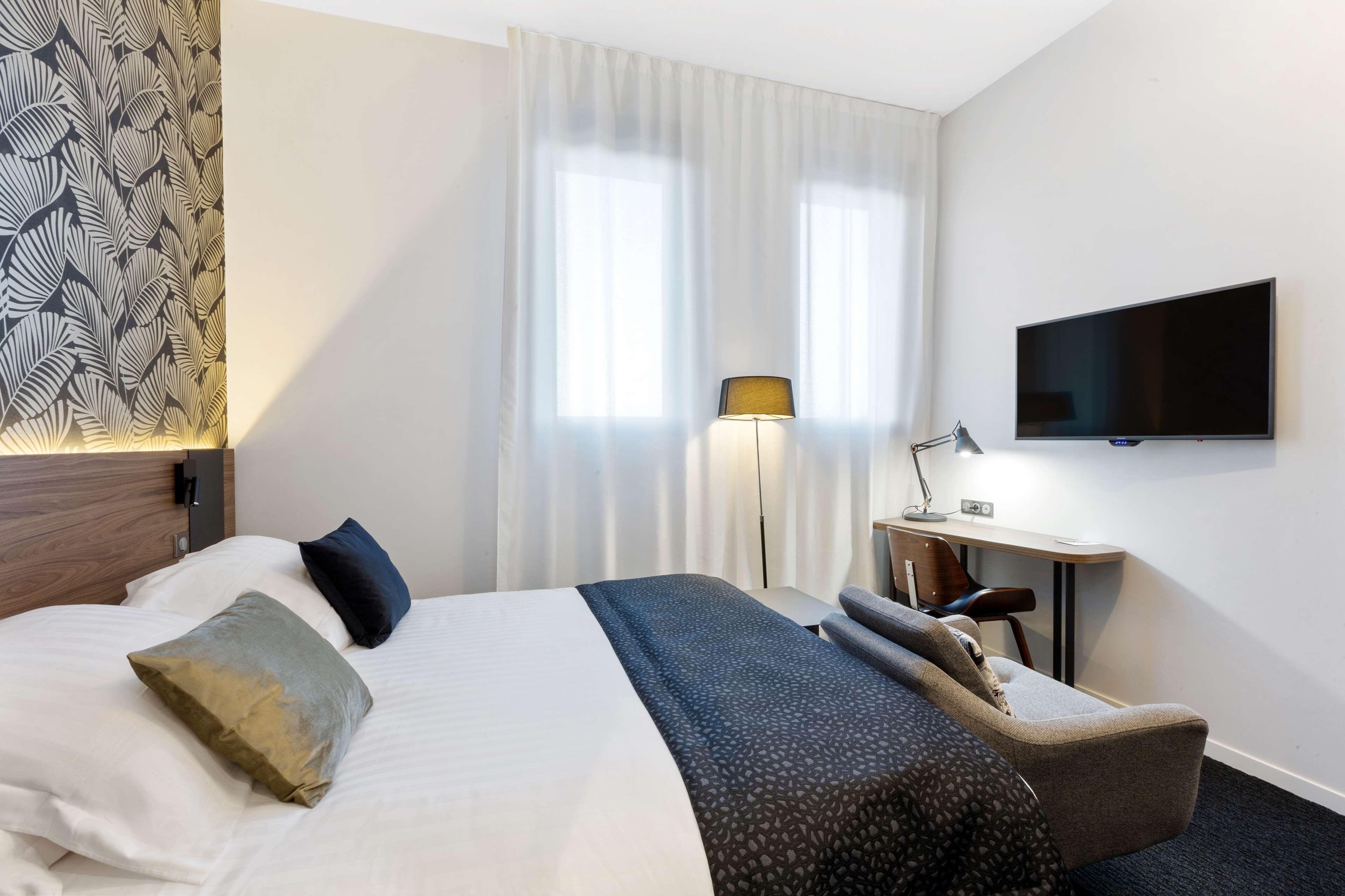A hotel room with a bed, a desk, a chair, a TV, and curtains.