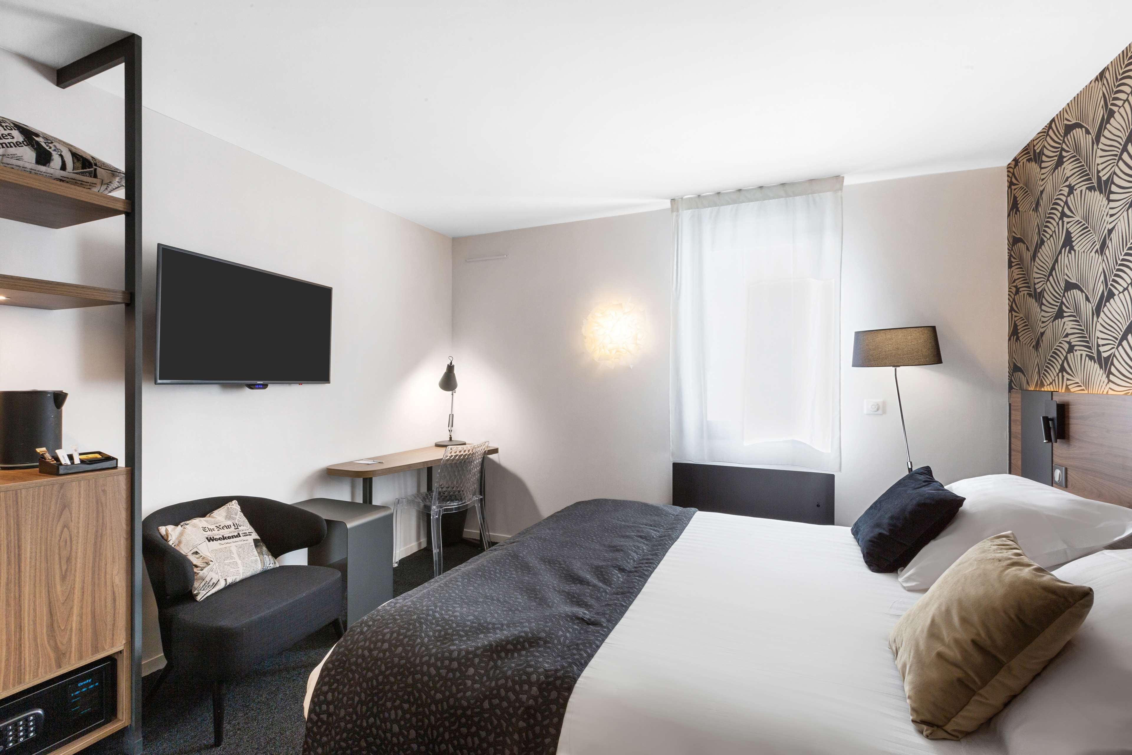 A hotel room with a bed, a desk with a chair, a television, and a bookshelf.