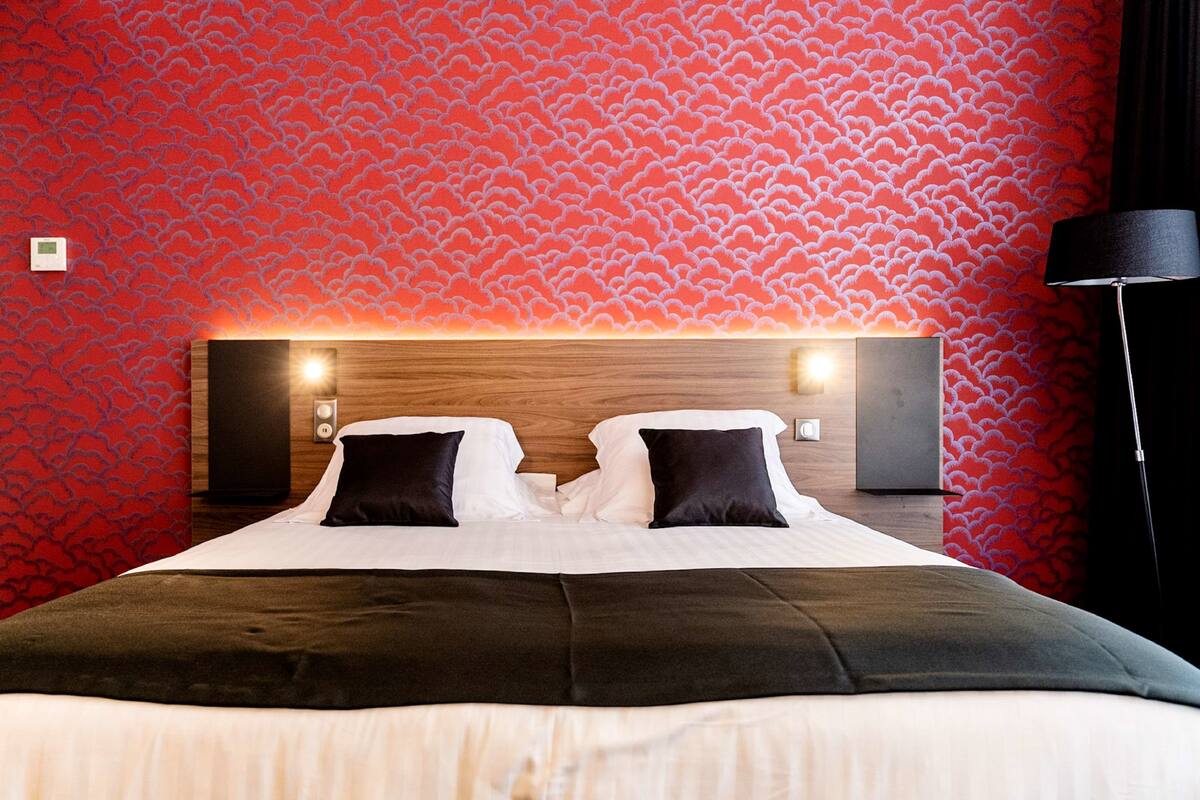 Quarto de hotel com uma cama grande, duas mesas de cabeceira e parede com padrão vermelho.