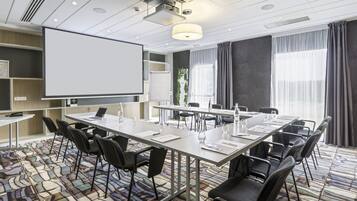 A conference room with a long table, chairs, a projector screen, and a large window with curtains.