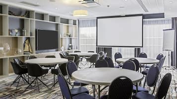 Un salón de conferencias con varias mesas y sillas, una pantalla grande y un proyector.