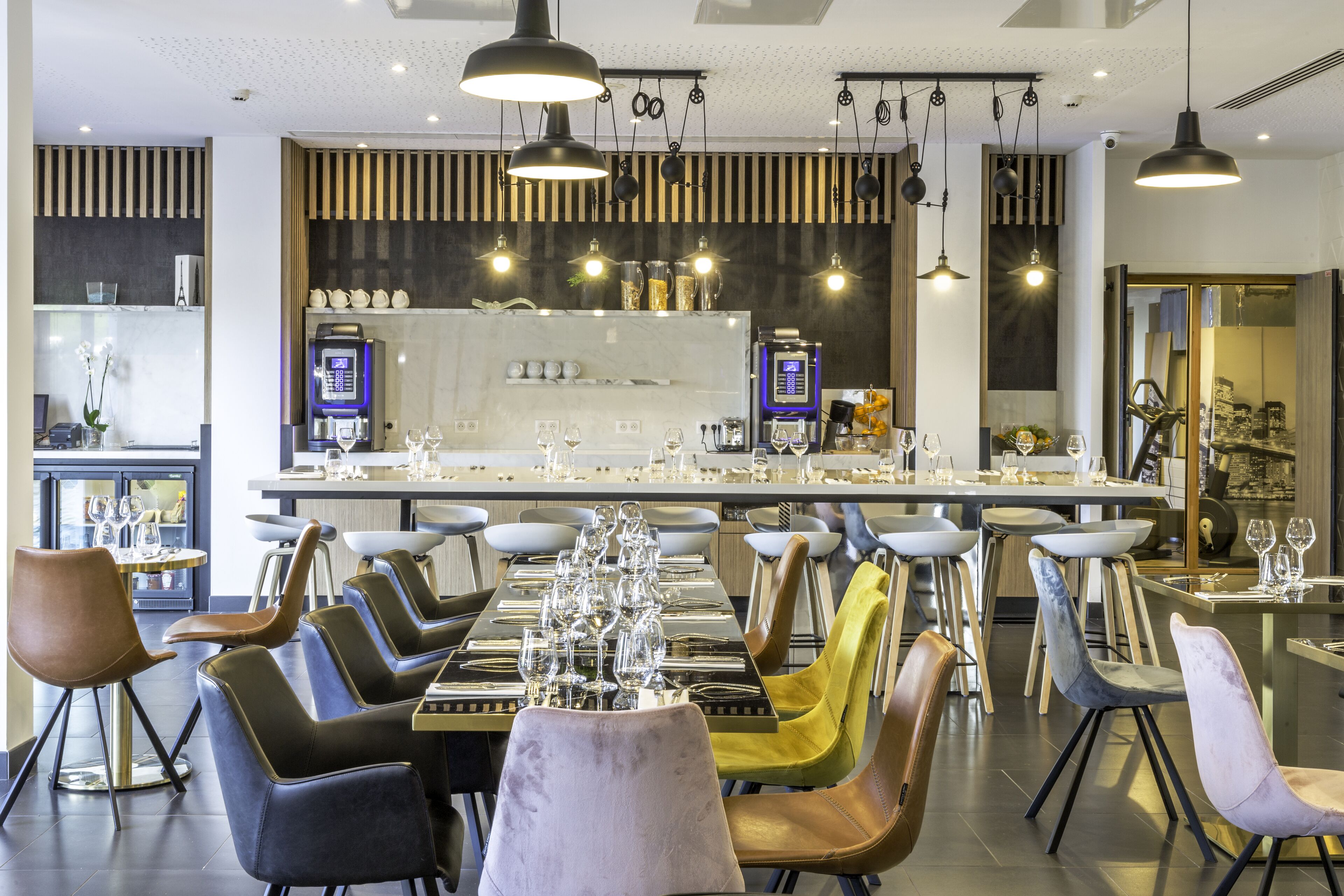Een modern restaurant met een lange gedeelde tafel, verschillende zithoeken en eigentijdse verlichtingsarmaturen.
