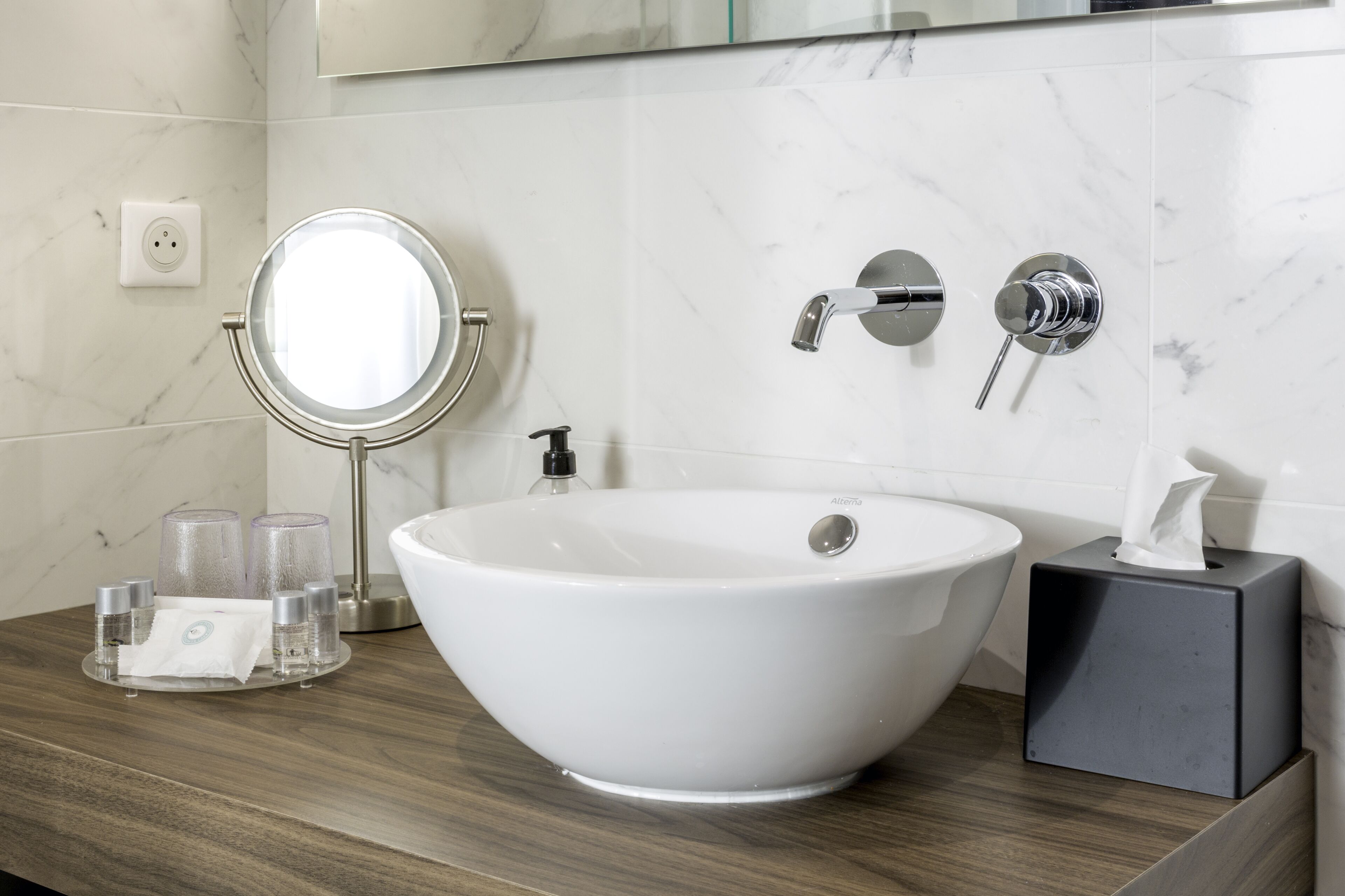 A modern bathroom with a white vessel sink, a round mirror, and a handheld showerhead.