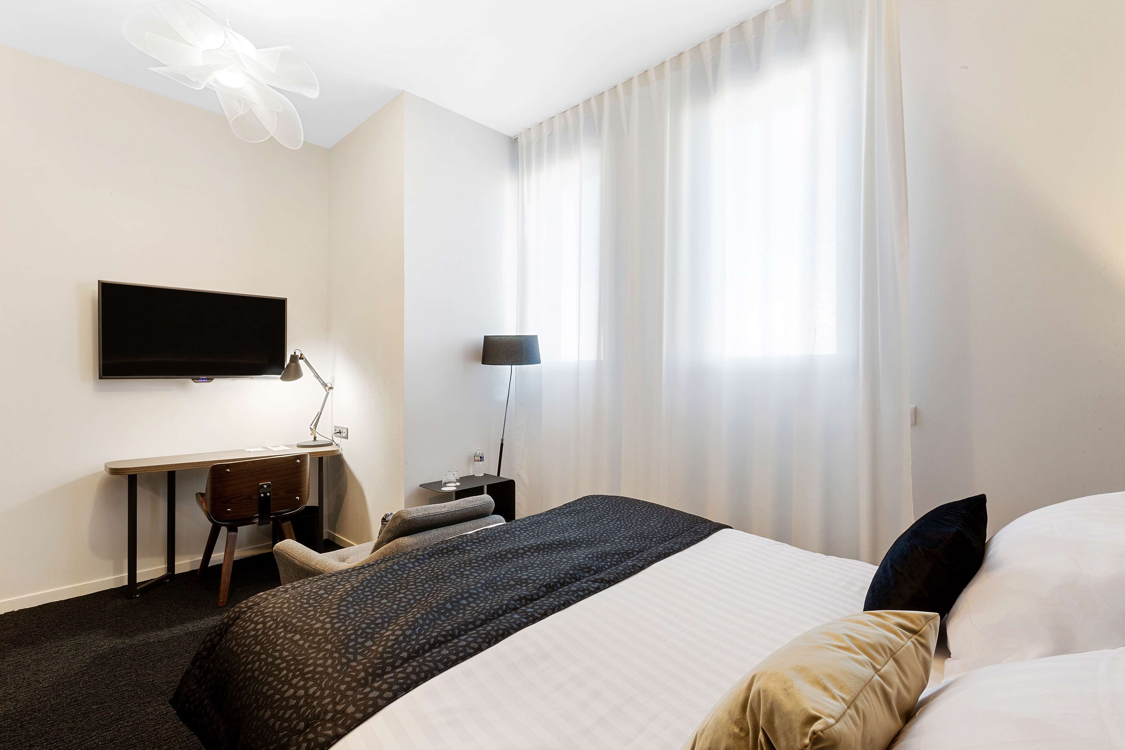 Een hotelkamer met een bed, een bureau, een stoel, een televisie en een raam met gordijnen.