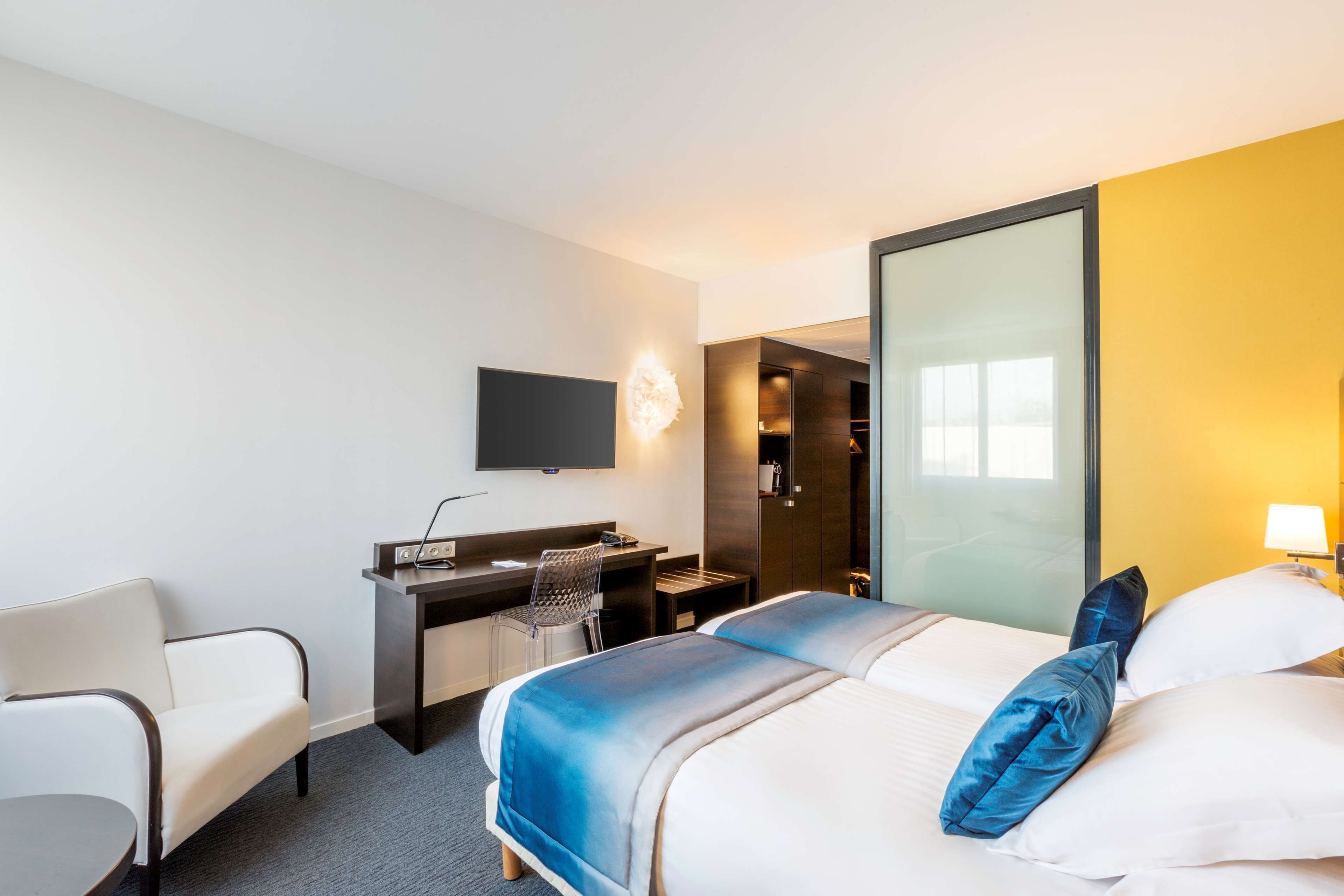 A hotel room with a bed, a desk, a chair, a TV, and a mirror.