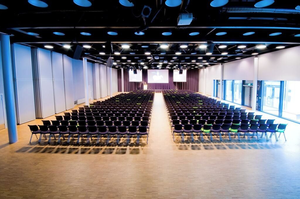 Un amplio y moderno salón de conferencias con filas de sillas mirando hacia un escenario.