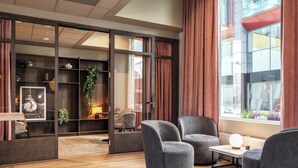 A modern room with a wooden floor, grey armchairs, a small table, and a bookshelf with plants. - Thon Hotel Ullevaal Stadion (Oslo)