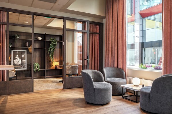 Una habitación moderna con suelo de madera, sillones grises, una pequeña mesa y una estantería con plantas.
