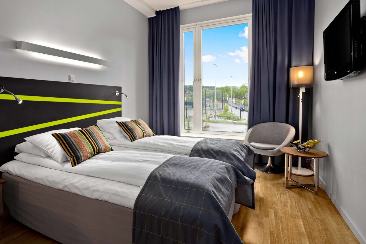 A hotel room with a bed, a chair, a TV, and a window with curtains.