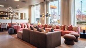 A modern hotel lobby with a large seating area, a bar, and large windows offering a view of the outdoors. - Thon Hotel Ullevaal Stadion (Oslo)