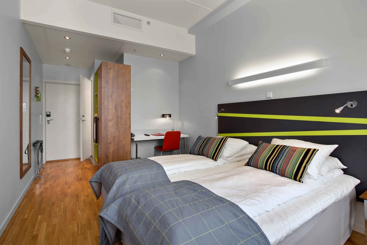 A modern hotel room with a large bed, a desk, and a chair.