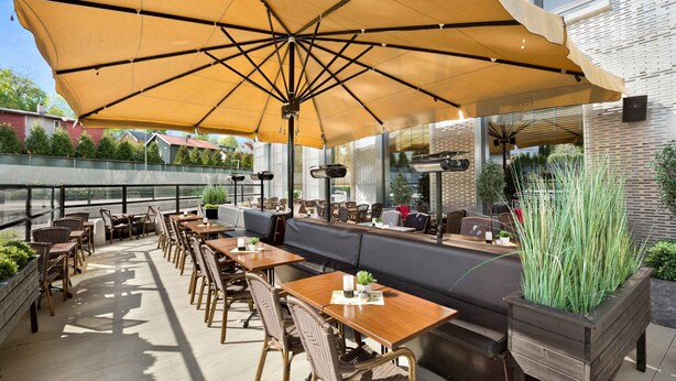 An outdoor seating area with tables and chairs, a large umbrella, and a view of the city. - Thon Hotel Ullevaal Stadion (Oslo)