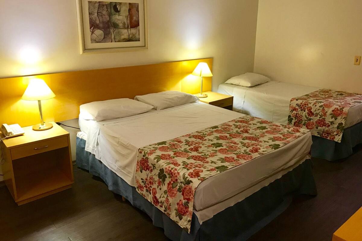 Een hotelkamer met twee bedden, een nachtkastje met een lamp, een klein tafeltje en een lijst met een foto aan de muur.