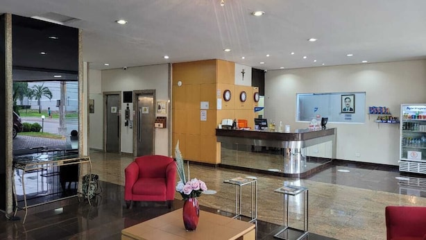 Un hall d’entrée moderne avec un comptoir d’accueil, un fauteuil rouge, un vase de fleurs et une machine à café.