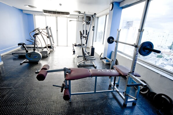 Un gimnasio con equipo de ejercicio, una banca y una ventana con vista a la ciudad.