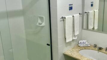 Uma casa de banho com chuveiro em cabine de vidro, lavatório com bancada de mármore e espelho sobre o lavatório.