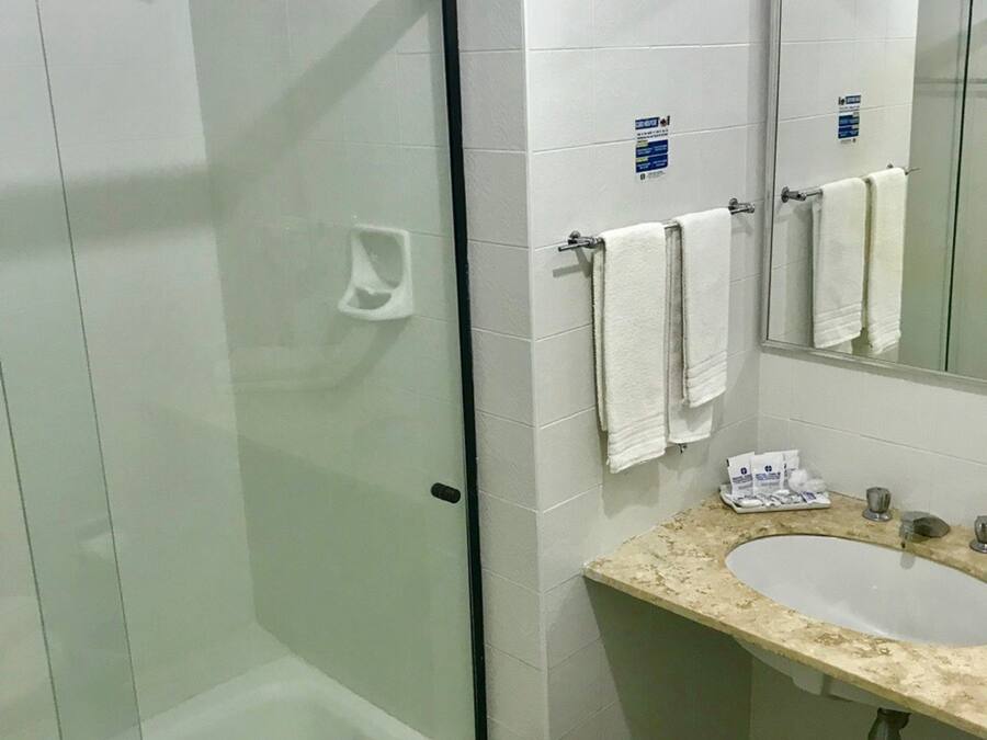 Une salle de bain dotée d’une douche à parois de verre, d’un lavabo avec un plan de travail en marbre et d’un miroir au-dessus du lavabo.