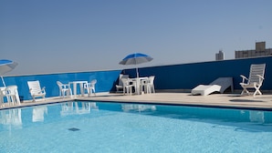 Une piscine aux eaux cristallines, bordée de chaises longues et de tables blanches, un mur bleu et un ciel dégagé.