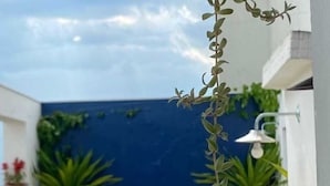 Une petite terrasse extérieure avec un banc en bois, des chaises en plastique blanches et des plantes en pot.