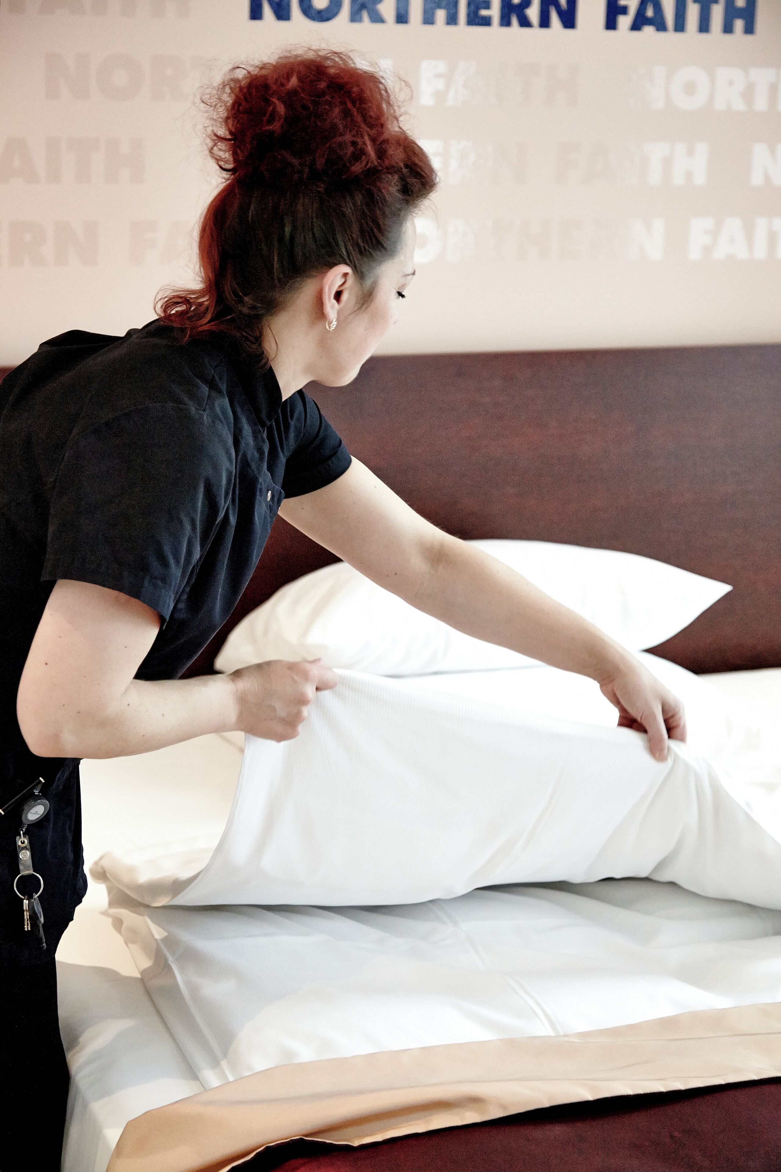 Une personne est en train de disposer un oreiller blanc sur un lit dont la tête de lit est marron.