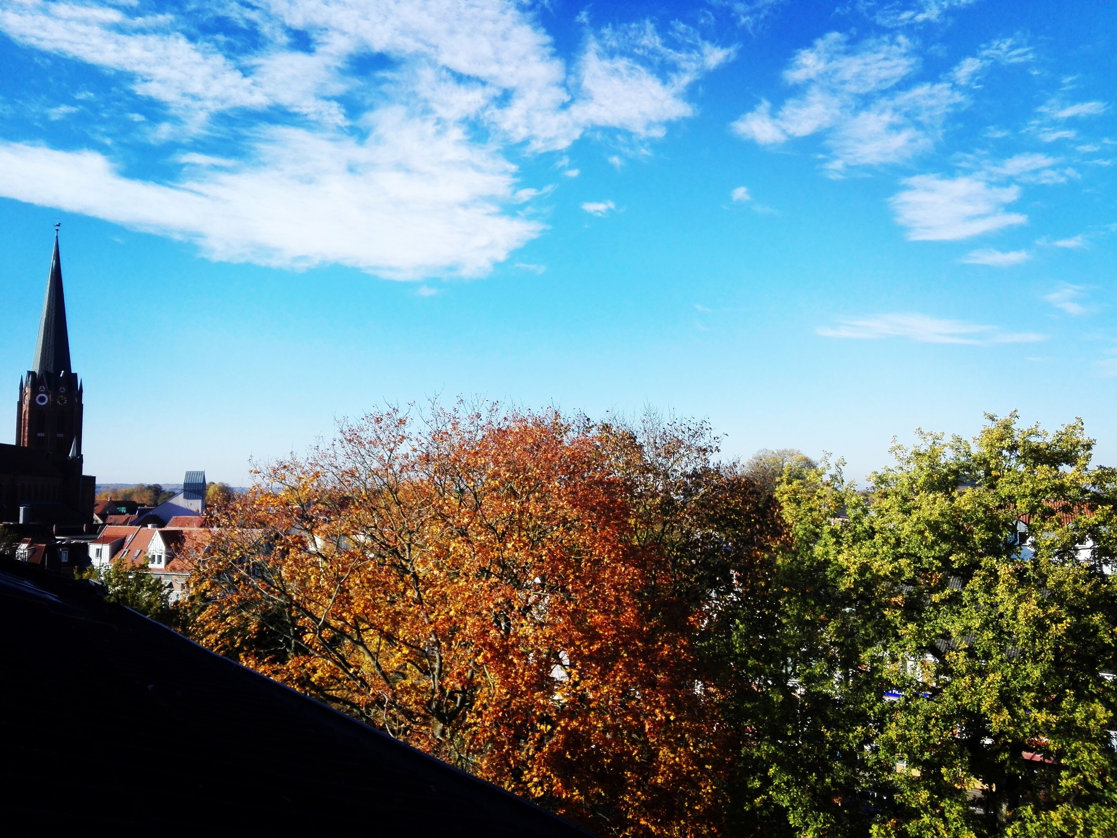 A church spire, autumn foliage, and a clear blue sky.