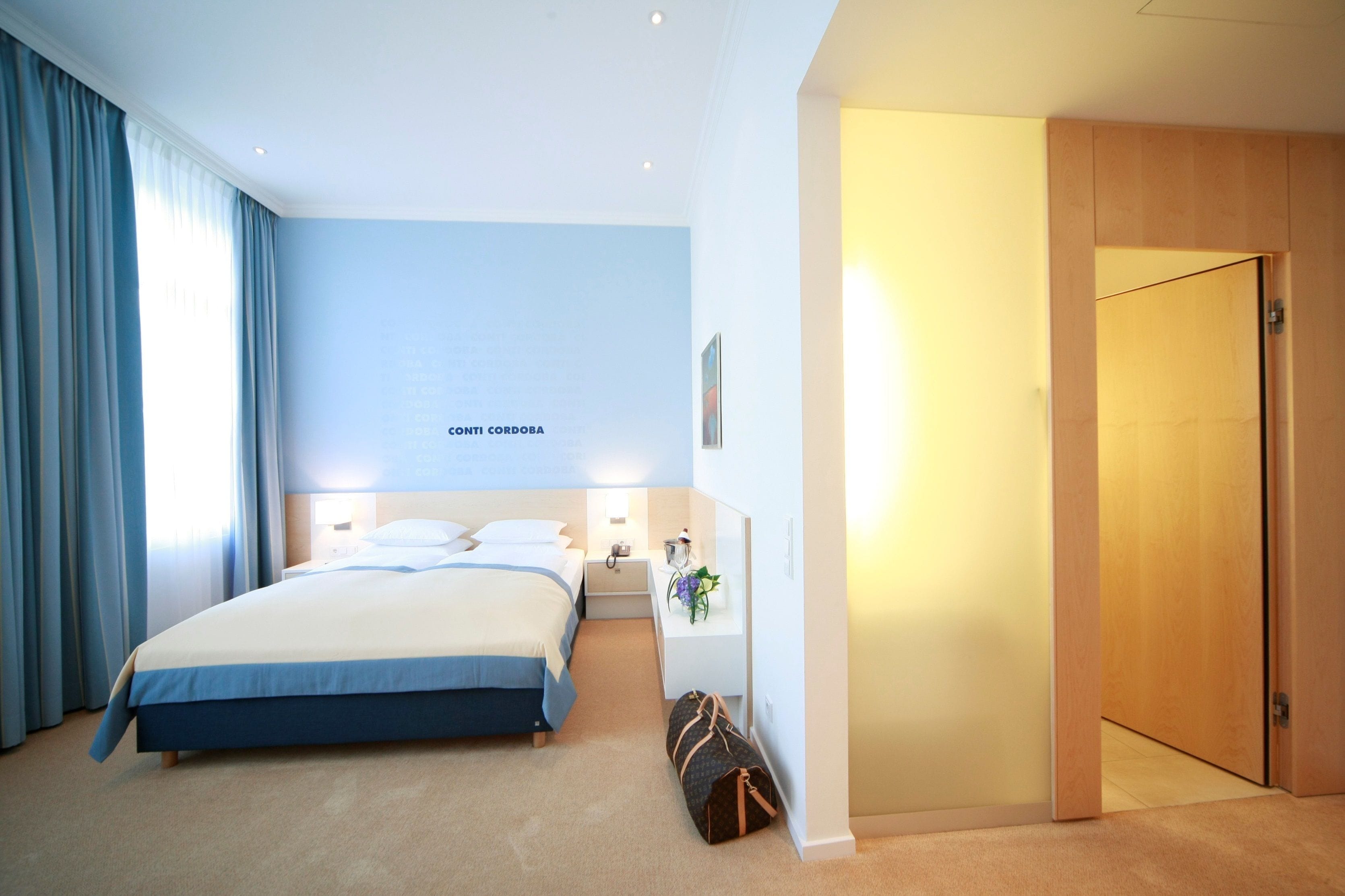 Ein Hotelzimmer mit einem großen Bett, einem Nachttisch, einer Lampe, einem Wandbild und einer Tür.