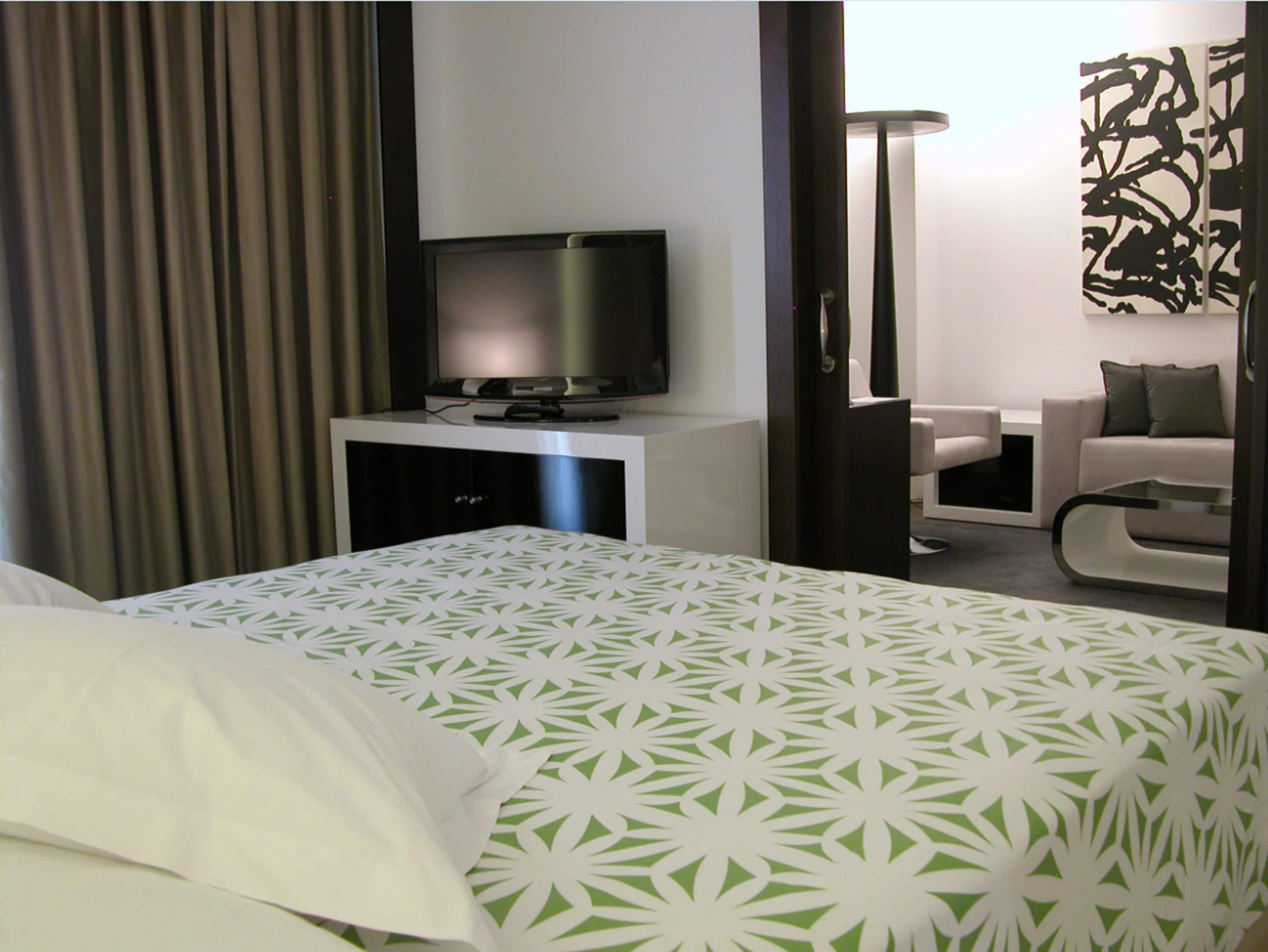 Habitación de hotel con cama, televisor sobre un mueble, escritorio y una silla.