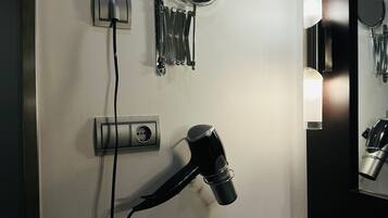 Un baño con secador de pelo, espejo redondo y lavamanos.