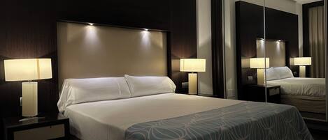 Una habitación de hotel con una cama grande, dos lámparas de noche, una mesita de noche y un espejo.
