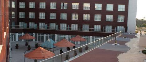A modern hotel with a red brick facade, multiple windows, and a covered outdoor area with umbrellas and potted plants.