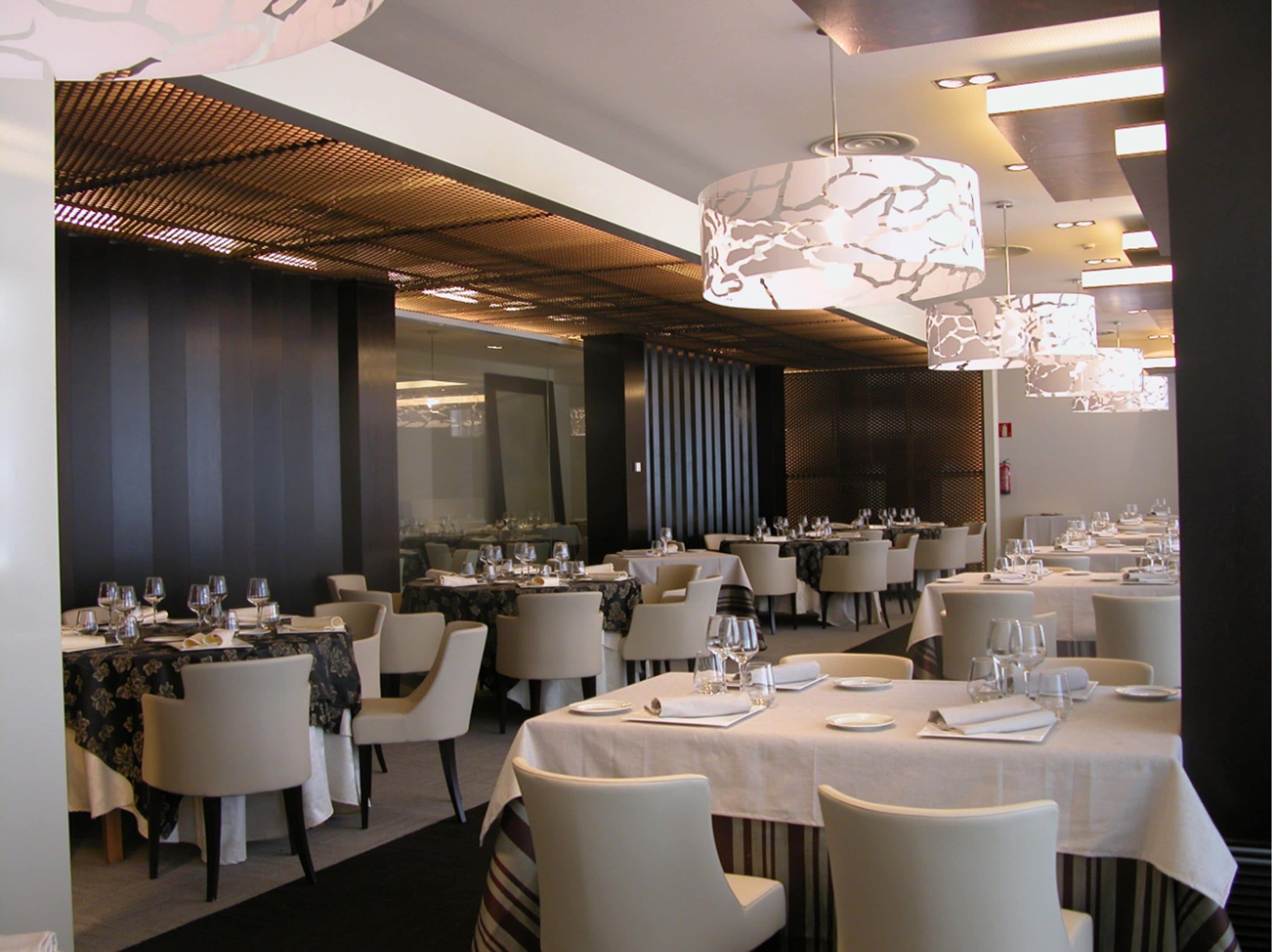 A restaurant with multiple tables set for dining, featuring a modern interior with patterned ceiling and ambient lighting.