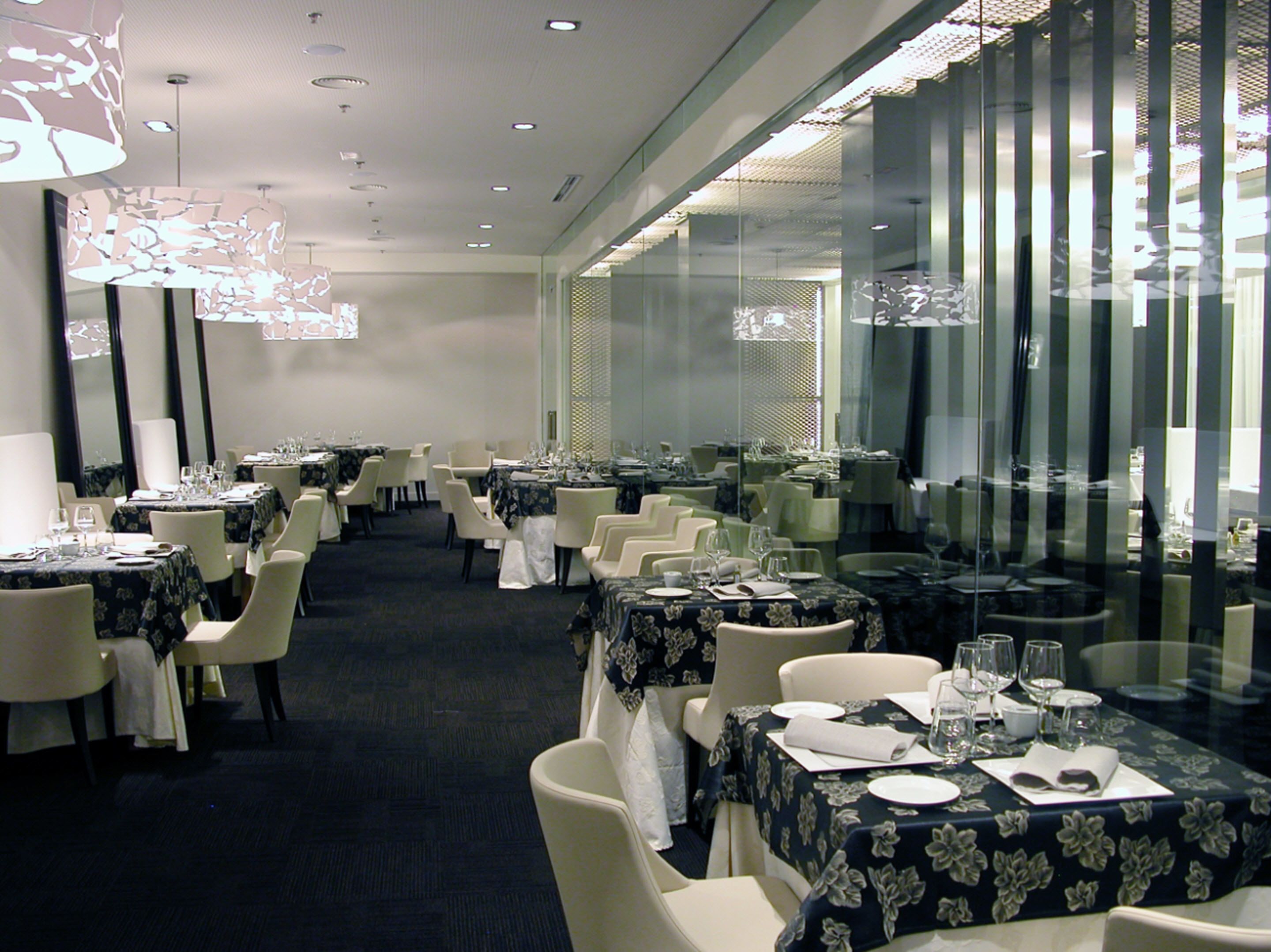 A dining area with multiple tables set for service, featuring a modern chandelier and glass partitions.