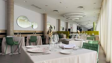 A restaurant with round tables, green chairs, and a modern ceiling design.