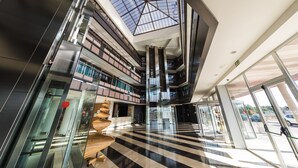 A modern multi-level atrium with glass railings, a central staircase, and a skylight. - Hotel Palacio Albacete & SPA (Albacete)