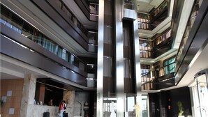 A modern hotel lobby with a central elevator, multiple floors, and a reception area. - Hotel Palacio Albacete & SPA (Albacete)